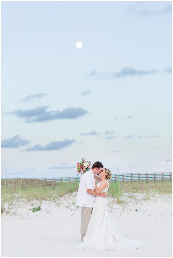 orange beach alabama destination wedding photo on sand dunes with fairytale wedding dress and white and pink floral design with succulents and moon in background