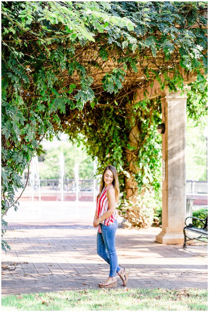 downtown senior session in front of greenery covered arch with girl in bright striped top