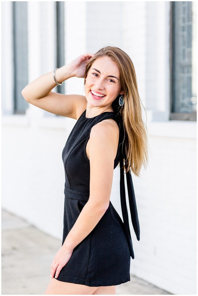 downtown senior session in front of white wall with girl in black romper