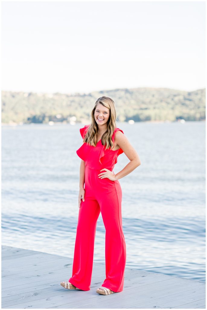 lake senior pictures on dock of girl in bright pink jumpsuit