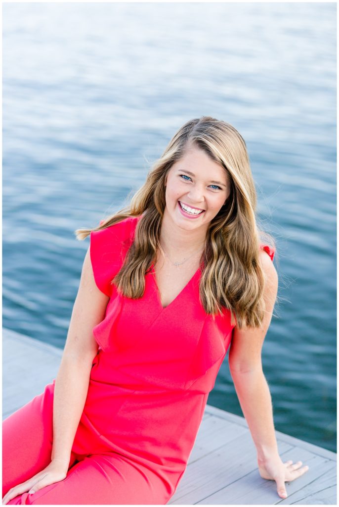lake senior pictures on dock of girl in bright pink jumpsuit