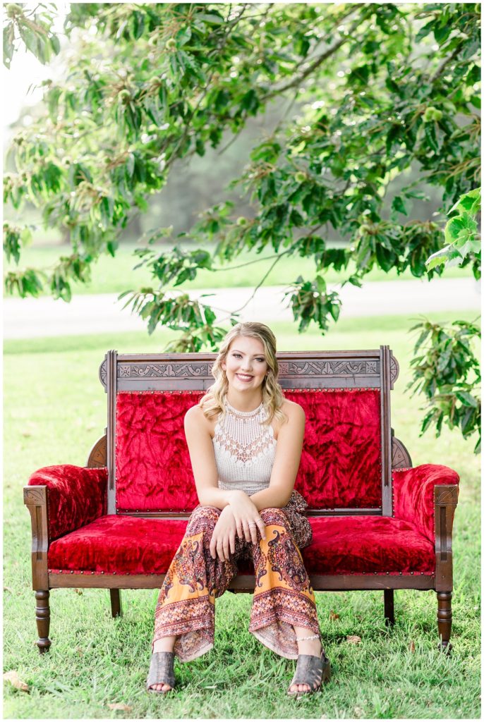 boho senior session with bright red couch, and red barn, and sunflowers