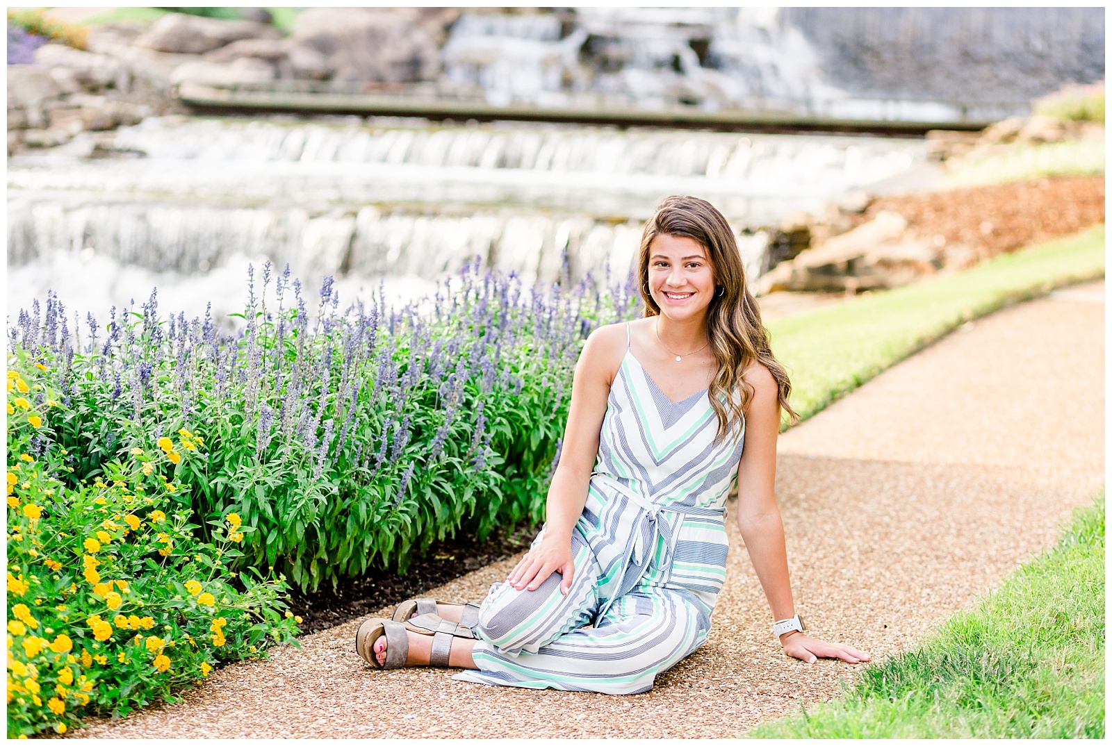 senior picture in striped jumpsuit by waterfall and flowers