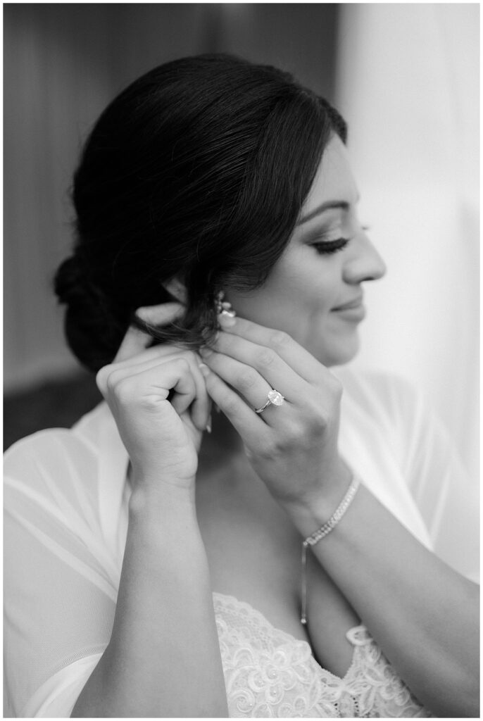 bride putting on earrings with oval engagement ring